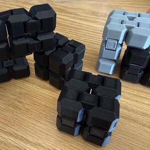 May include: A collection of articulated fidget toys constructed from interconnected black and grey geometric blocks. These modular objects feature a repeating pattern of linked segments that allow for flexible movement and manipulation by hand.
