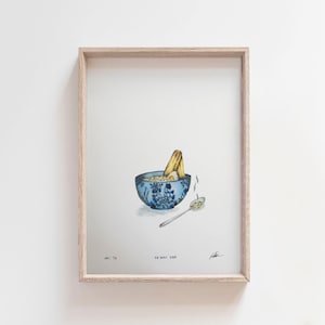 May include: A watercolour painting of a bowl of ramen with a blue and white floral pattern. The bowl is filled with noodles, broth, and a soft-boiled egg. A single piece of ramen noodle sticks out of the bowl. A silver spoon is next to the bowl. The painting is signed and numbered.