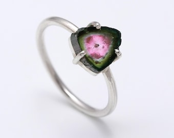 Könnte beinhalten: Ein Silberring mit einem rohen, dreieckigen Wassermelonen-Turmalin-Edelstein in einer Vier-Krappen-Fassung. Der Stein zeigt ein leuchtend rosa Zentrum, das von einem dunkelgrünen Rand umgeben ist, gehalten von einer dünnen, polierten Silberschiene.