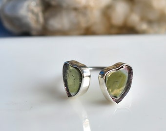 May include: An open-style ring featuring two heart-shaped, translucent pale green stones set in polished silver bezels. The band is thin and metallic, connecting the two stones which are positioned to face each other with a small gap in between.