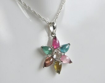 May include: A silver necklace featuring a flower-shaped pendant. The pendant consists of a central clear round gemstone surrounded by six pear-shaped gemstones in various colors, including pink, teal, green, brown, yellow, and light pink.