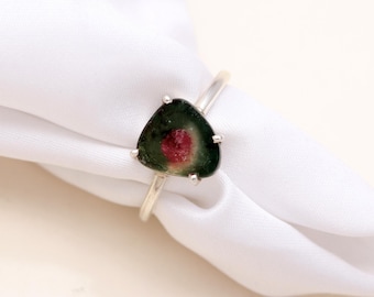 Könnte beinhalten: Ein Ring mit einem dreieckigen Wassermelonen-Turmalin-Edelstein, der einen dunkelgrünen äußeren Rand und ein leuchtend rosa Zentrum aufweist. Der Stein ist in eine schlichte, silberfarbene Metallschiene mit vier kleinen Krappen gefasst.