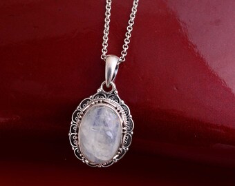 May include: A silver pendant necklace featuring an oval-shaped moonstone cabochon set in a decorative, filigree-style metal frame. The pendant hangs from a delicate silver chain, showcasing the iridescent, milky white surface of the stone.
