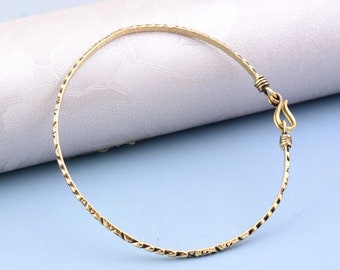 Puede incluir: Una pulsera circular fina de metal en tono dorado con una superficie texturizada y martillada. La pulsera cuenta con un mecanismo de cierre de gancho sencillo, con pequeños detalles de alambre enrollado que aseguran el gancho.