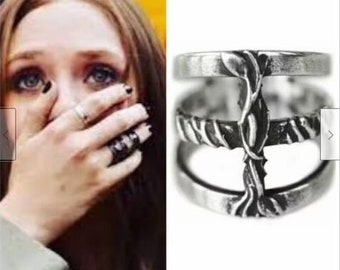 May include: A silver-toned metal ring featuring a multi-band design connected by a vertical element that resembles a thorny vine or branch. The ring has a distressed, antique finish with dark recessed areas and polished highlights on the surface.