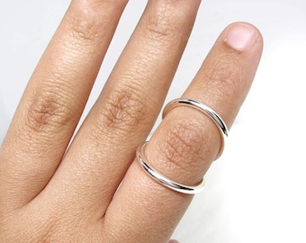 May include: A pair of smooth, polished silver-tone rings worn on a single finger. One ring is positioned at the base of the finger, while the second ring is placed above the knuckle, creating a stacked appearance with a gap between them.