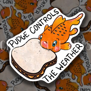 May include: A sticker featuring a cartoon orange fish with a large eye, eating a peanut butter and jelly sandwich. The text "Pudge Controls The Weather" is written around the fish and sandwich.