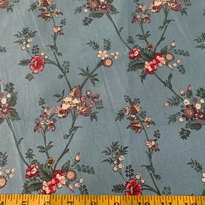May include: Blue fabric with a floral pattern featuring pink, white, and purple flowers. The fabric has a subtle texture and a light blue background.