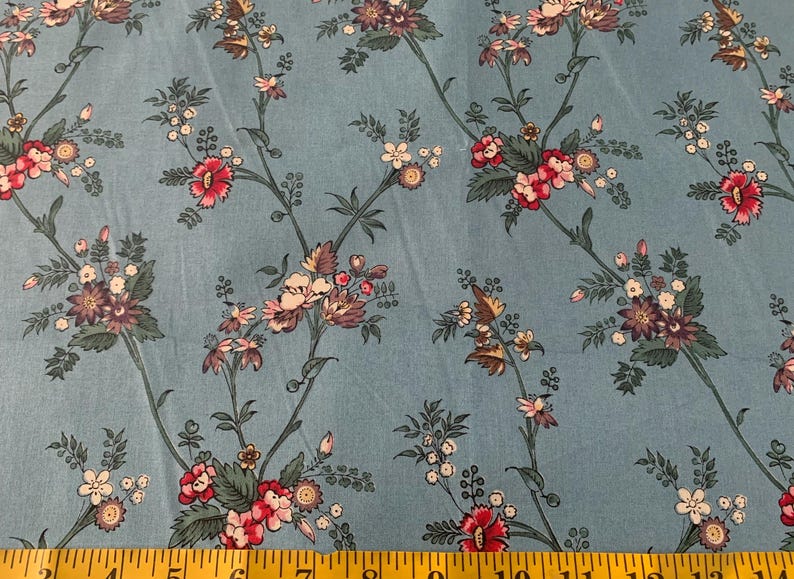 May include: Blue fabric with a floral pattern featuring pink, white, and purple flowers. The fabric has a subtle texture and a light blue background.