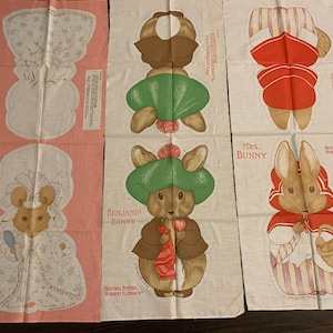 May include: Three fabric panels featuring illustrations of characters from Beatrix Potter's stories. One panel shows a mouse, another features Benjamin Bunny, and the third depicts Mrs. Bunny. The panels are in shades of pink and white.