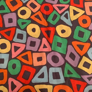 May include: A colourful fabric with a repeating pattern of geometric shapes. The shapes are in shades of red, orange, yellow, green, blue, and purple. The background is a dark brown.
