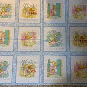 May include: A fabric panel with twelve illustrated squares depicting rabbits and other animals in a garden. Each square has a light blue border with a floral design. The illustrations are in pastel colours.