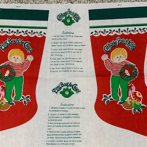 May include: A fabric panel with instructions for making Christmas stockings. The panel features two red stockings with green trim, each with a different design. One stocking features a girl with a red dress and a white hat, holding a Christmas tree. The other stocking features a boy with a red shirt and a green hat, holding a Christmas tree. The text on the panel reads "Our First Christmas".