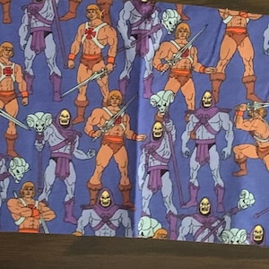 May include: A blue fabric with a repeating pattern of He-Man and Skeletor characters from the Masters of the Universe cartoon. The characters are in their iconic poses, with He-Man holding his sword and Skeletor holding his staff.