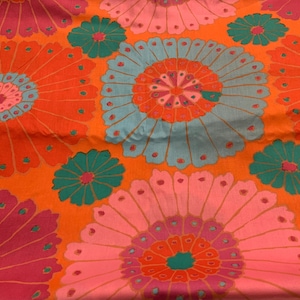 May include: A colourful fabric with a repeating floral design. Large, stylised flowers in shades of orange, pink, teal, and magenta are set against an orange background. The design has a retro, psychedelic aesthetic.