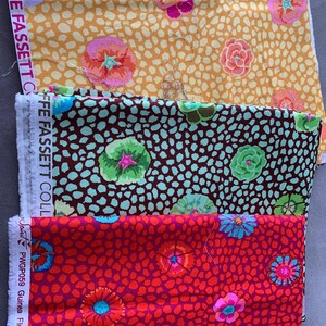 May include: Three fabric swatches with floral designs. The top swatch is mustard yellow with pink and orange flowers. The middle swatch is brown with teal and green flowers. The bottom swatch is red with pink and blue flowers. The text "KAFFE FASSETT" is visible.
