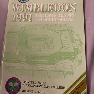 Peut inclure: Programme souvenir vert clair des Championnats de Wimbledon 1991. La couverture présente le logo de Wimbledon, l'année et une illustration du complexe de tennis. Le texte comprend "Lundi 24 juin - Premier jour".
