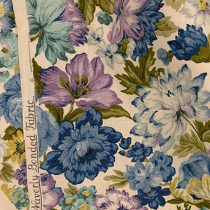May include: Close-up of floral fabric with large blue, purple, and white flowers. The fabric has a cream background and green leaves. A white strip on the left side reads "A Waverly Bonded Fabric" and "Register".