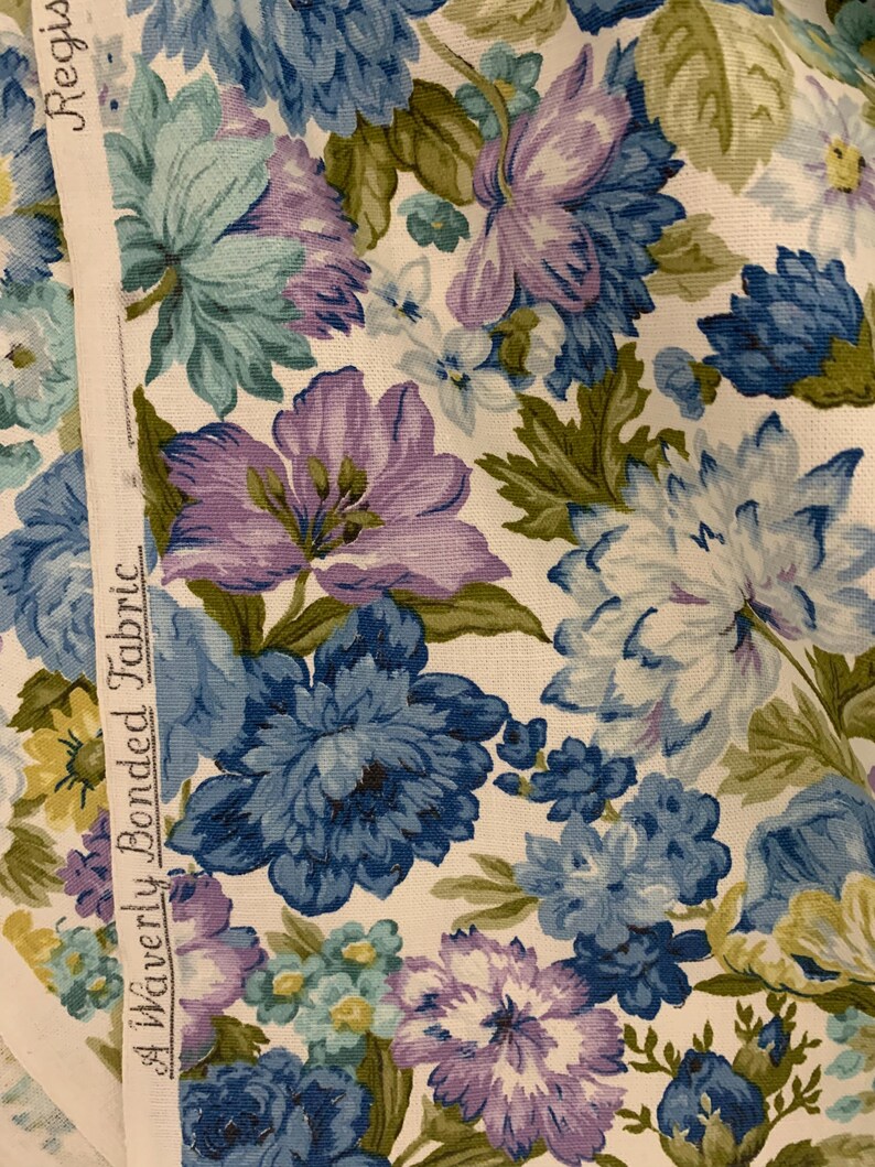 May include: Close-up of floral fabric with large blue, purple, and white flowers. The fabric has a cream background and green leaves. A white strip on the left side reads "A Waverly Bonded Fabric" and "Register".