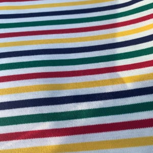 May include: Close-up of a fabric with horizontal stripes in various colours. The stripes alternate between white, red, yellow, green, and navy blue. The fabric appears to be a knit or woven material.