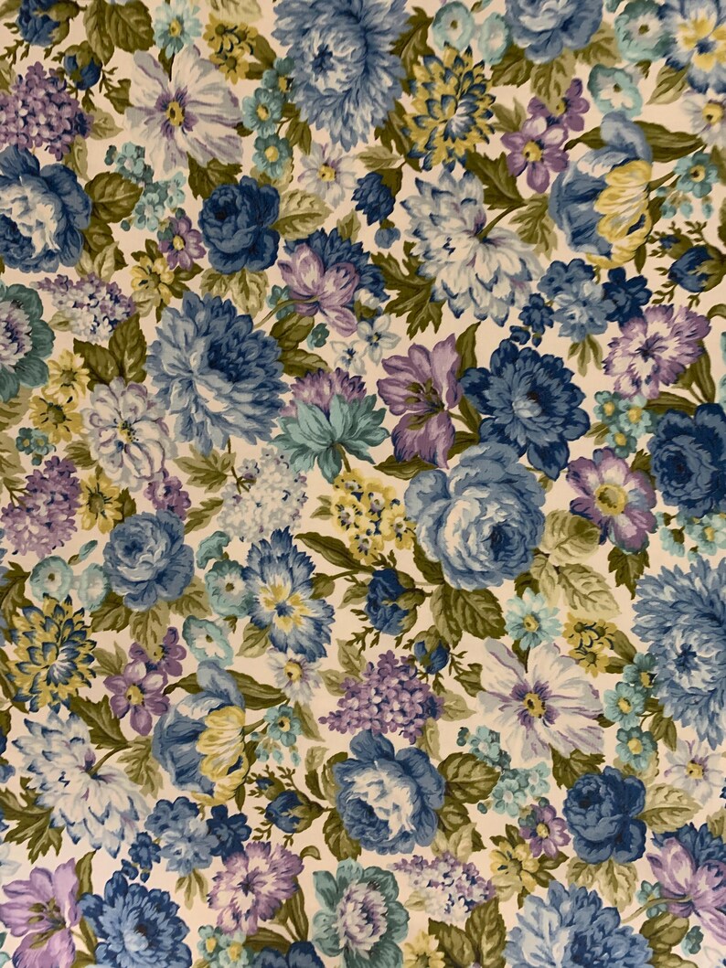 May include: Floral fabric featuring a repeating pattern of blue, purple, and yellow flowers with green leaves on a cream background. The flowers include roses, hydrangeas, and other blooms.