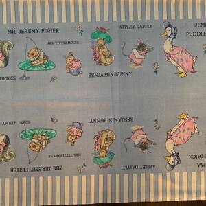 May include: Light blue fabric featuring illustrations of Beatrix Potter characters, including Peter Rabbit, Jemima Puddle-Duck, and Benjamin Bunny. The fabric has vertical white stripes and character names.