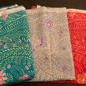 May include: Three patterned fabric pieces. One is teal with yellow and pink flowers, another is grey with purple flowers, and the third is red with white flowers. The fabric is labelled "Kaffe Fassett Collective".