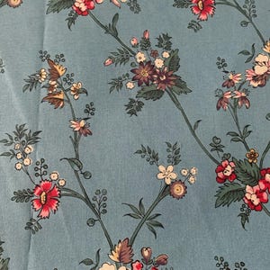 May include: A blue fabric with a floral pattern. The flowers are pink, white, and purple. The fabric has a subtle texture.