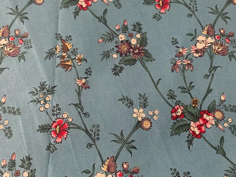 May include: A blue fabric with a floral pattern. The flowers are pink, white, and purple. The fabric has a subtle texture.