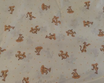 May include: A light cream-colored fabric featuring a repeating pattern of Tigger from Winnie the Pooh in various poses. The orange and black striped character is interspersed with small, scattered yellow triangles across the entire surface.