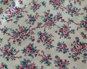May include: A white fabric with a repeating pattern of pink and purple floral bouquets. The bouquets are arranged in a diagonal pattern and are surrounded by small green leaves.