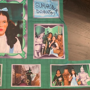 May include: A green fabric panel featuring images from the movie "The Wizard of Oz." The panel includes a portrait of Dorothy, scenes with the Tin Man, Scarecrow, and Cowardly Lion, and the text "Surrender Dorothy."