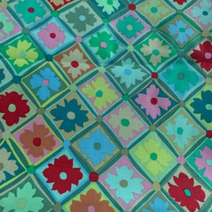 May include: A vibrant floral fabric with a repeating pattern of flowers enclosed in diamond shapes. The flowers are in shades of red, pink, yellow, and blue, set against a green and tan background. The design has a retro, vintage feel.