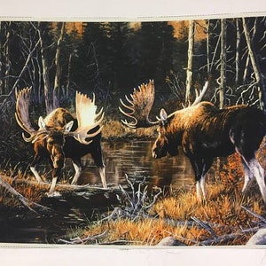 May include: A fabric panel depicting two moose in a woodland setting. The moose, with impressive antlers, are positioned near a stream, surrounded by trees and autumnal colours. The artwork is rendered in a realistic style with detailed animal and environment depictions.