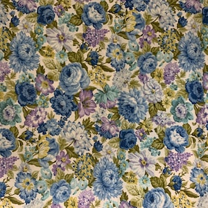 May include: Floral fabric featuring a dense pattern of blue, purple, and yellow flowers on a cream background. The design includes various flower types, such as roses and hydrangeas, with green foliage. The fabric has a vintage aesthetic.