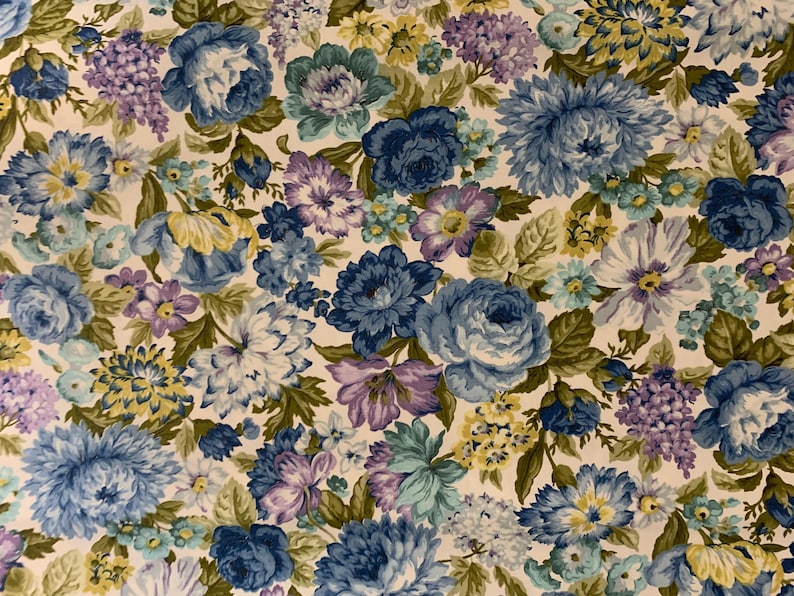 May include: Floral fabric featuring a dense pattern of blue, purple, and yellow flowers with green leaves on a cream background. The flowers include roses, hydrangeas, and other blooms, creating a vintage aesthetic.