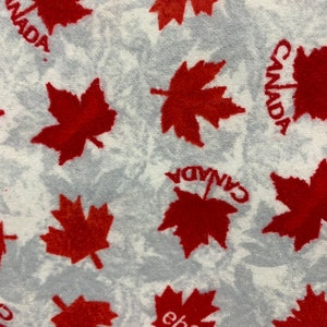 May include: White fabric with a repeating pattern of red maple leaves and the word "CANADA" printed in black. The fabric has a fuzzy texture.
