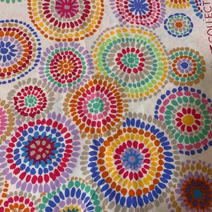 May include: White fabric featuring a vibrant pattern of multi-coloured dotted circles. The circles are in shades of pink, orange, yellow, green, blue, and purple. The fabric has a bright appearance, suitable for various craft projects.