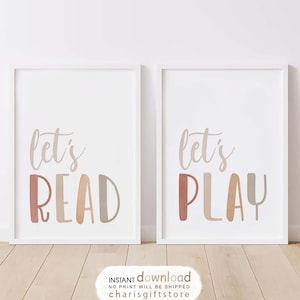 May include: Two framed art prints with the words "let's READ" and "let's PLAY" in a playful font. The text is in shades of brown, beige, and red. The frames are white, and the background is a soft white.