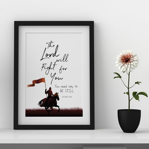 May include: A framed print with the text "The Lord will Fight for You" and an illustration of a person on horseback holding a flag. A black lamp and a potted flower are on the shelf.