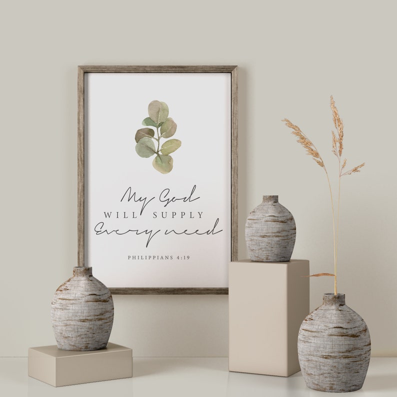 May include: A framed print with a watercolor illustration of a eucalyptus branch and the text "My God will supply every need Philippians 4:19". The print is displayed on a white wall with two decorative vases and a dried grass arrangement.