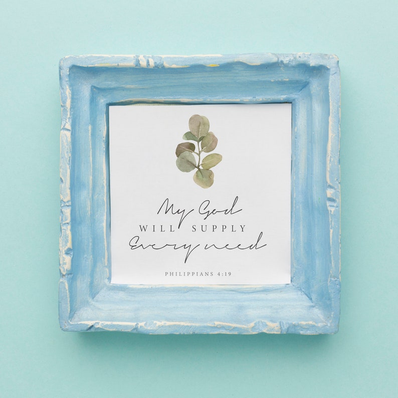 May include: A light blue frame with a white background and a watercolor illustration of a eucalyptus branch. The text "My God will supply every need" is written in black cursive font. The text "Philippians 4:19" is written in black font below the cursive text.
