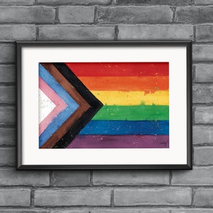 May include: A framed watercolor painting of a pride flag with a rainbow stripe design and a black triangle with additional stripes of brown, blue, light blue, and pink. The flag is on a white background with a few specks of paint.