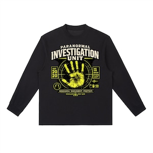 May include: A black long-sleeve shirt featuring a yellow graphic of a handprint inside a radar circle. Text includes PARANORMAL INVESTIGATION UNIT, EST. 2020, WE SEE WHAT OTHERS CAN'T, RESEARCH. DOCUMENT. PROTECT., and STAY ALERT STAY SAFE with icons.