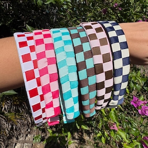 May include: A set of six headbands featuring a repeating checkered pattern in various color combinations including red and white, hot pink and light pink, turquoise and white, brown and turquoise, brown and light pink, and navy blue and white.