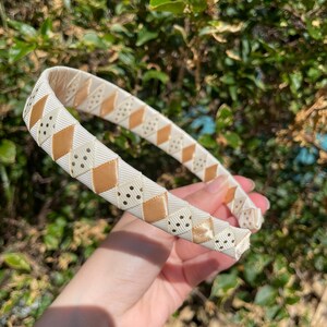May include: A white headband with a brown and white geometric pattern. The headband is made of a soft, flexible material and is perfect for adding a touch of style to any outfit.