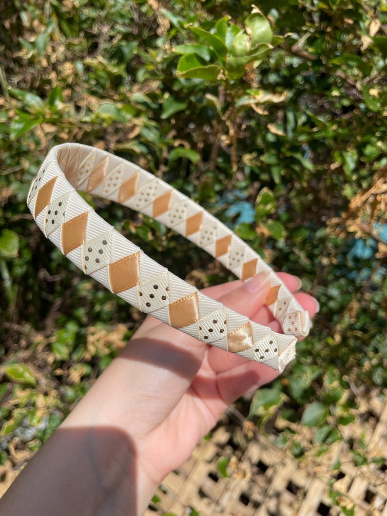May include: A white headband with a brown and white geometric pattern. The headband is made of a soft, flexible material and is perfect for adding a touch of style to any outfit.