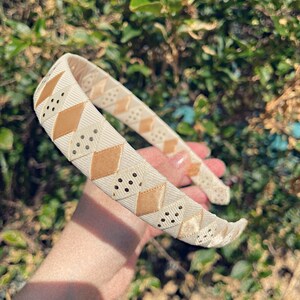 May include: A white headband with a brown and white geometric pattern. The headband is made of a soft, flexible material and has a comfortable fit.