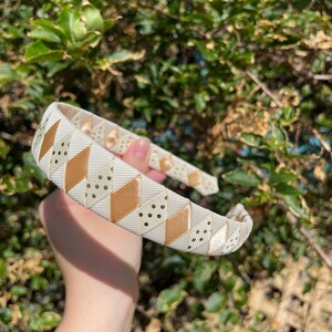 May include: A white headband with a geometric pattern of gold and white diamonds. The headband has small white polka dots on the gold diamonds.