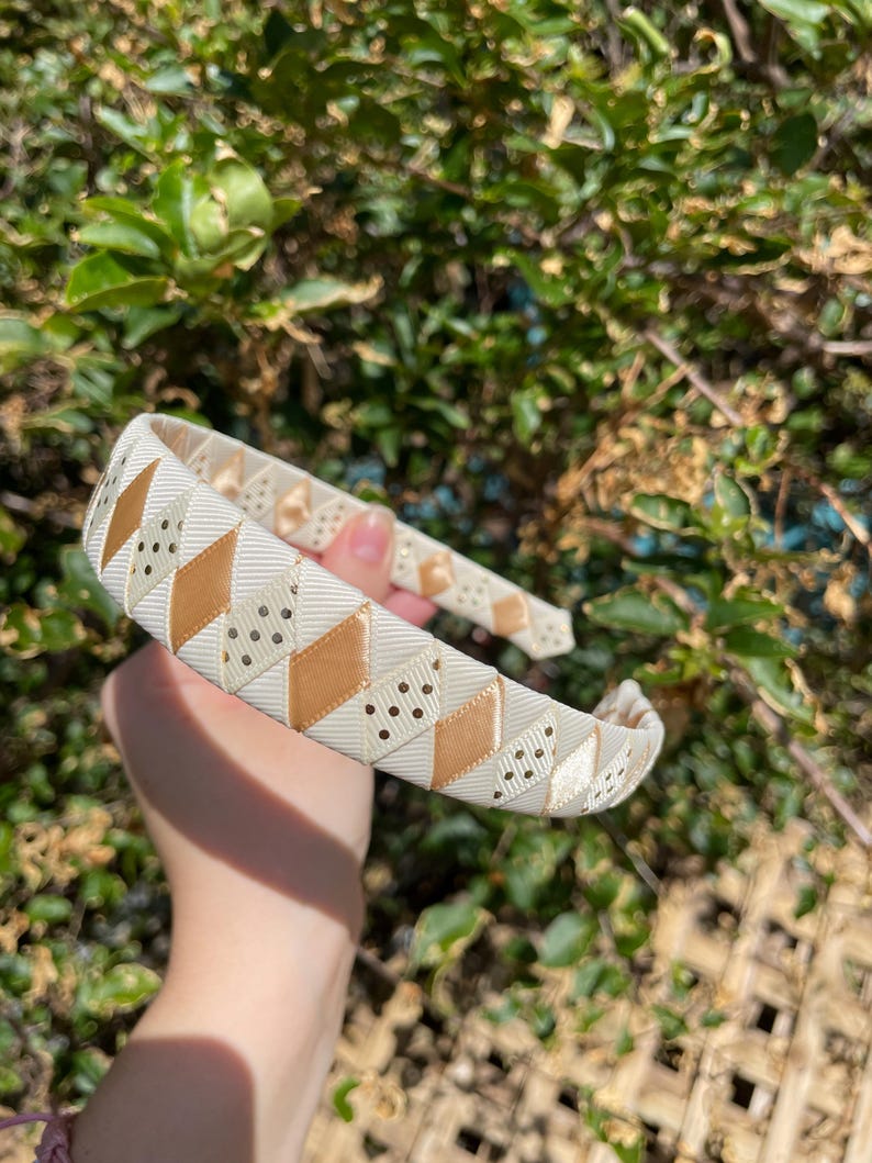 May include: A white headband with a geometric pattern of gold and white diamonds. The headband has small white polka dots on the gold diamonds.